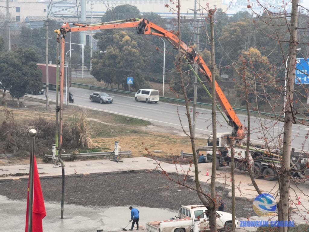 Concrete pump truck with extended boom delivering concrete at EV charging station construction site