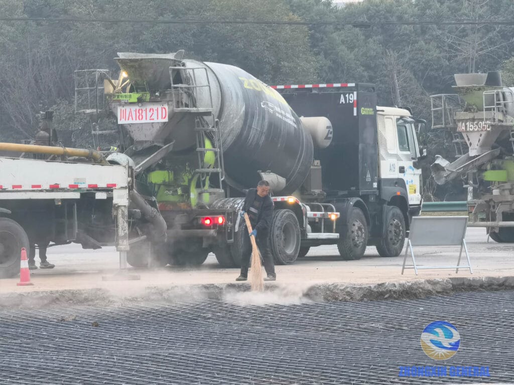 Concrete mixer trucks waiting at roadside with completed steel reinforcement grid in foreground at EV charging station