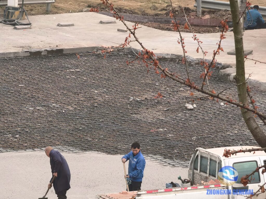 Aerial view from fourth-floor office showing half-completed concrete pour and remaining rebar grid at charging station
