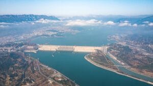Aerial panoramic view of Three Gorges Dam across full width with Yangtze River reservoir and upstream city visible in background