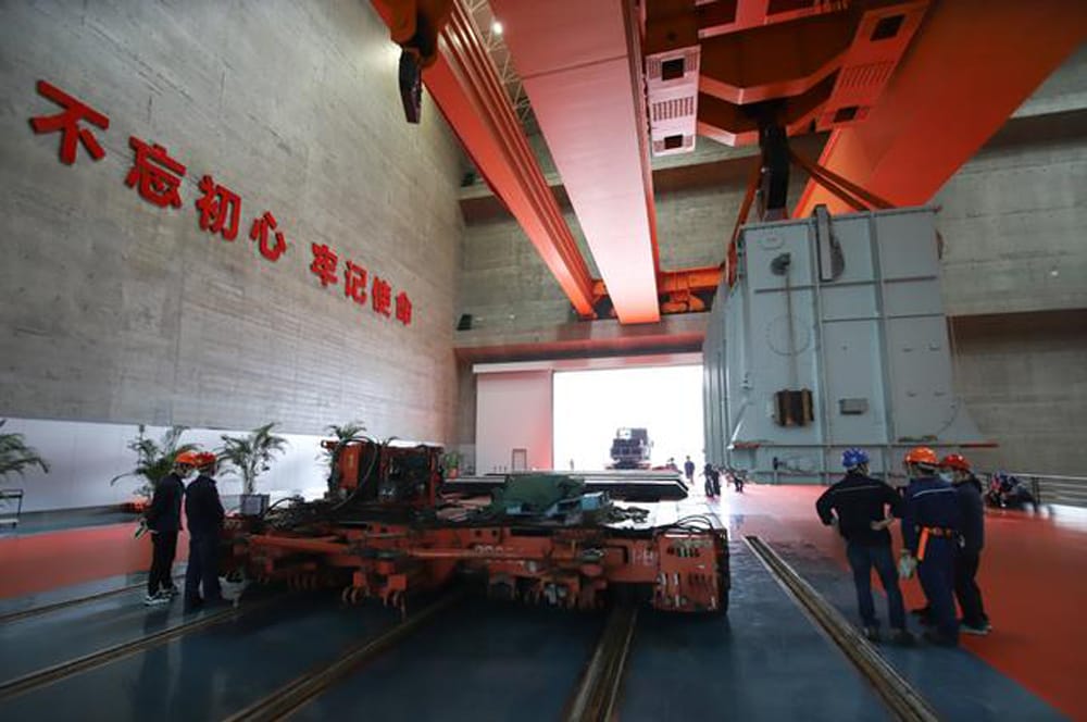 Overhead bridge crane inside Three Gorges power station lifting 500 kV transformer onto rail transfer trolley, 2020