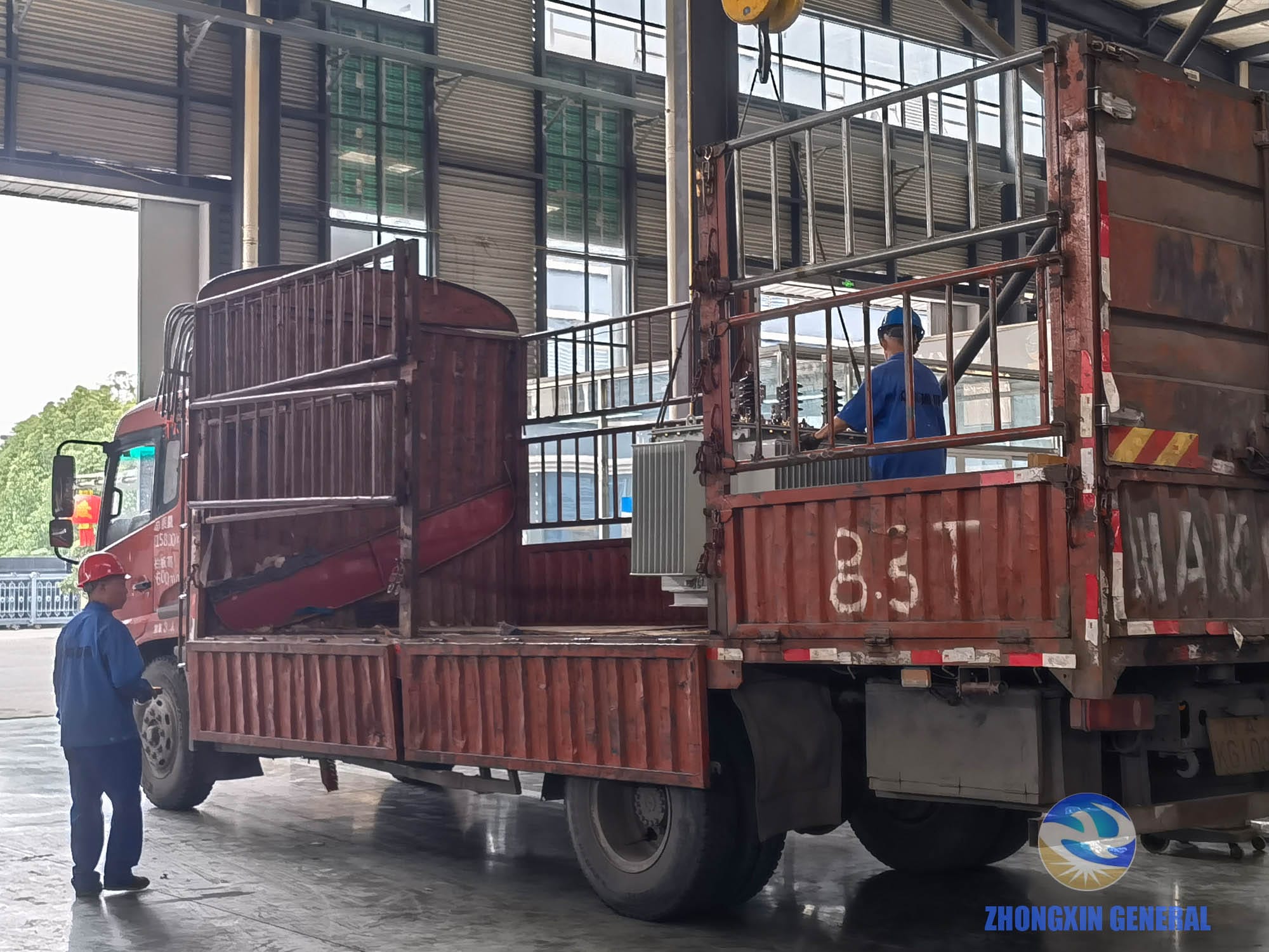 Oil-immersed distribution transformers being crane-loaded onto truck inside factory workshop — Zhongxin General Sichuan