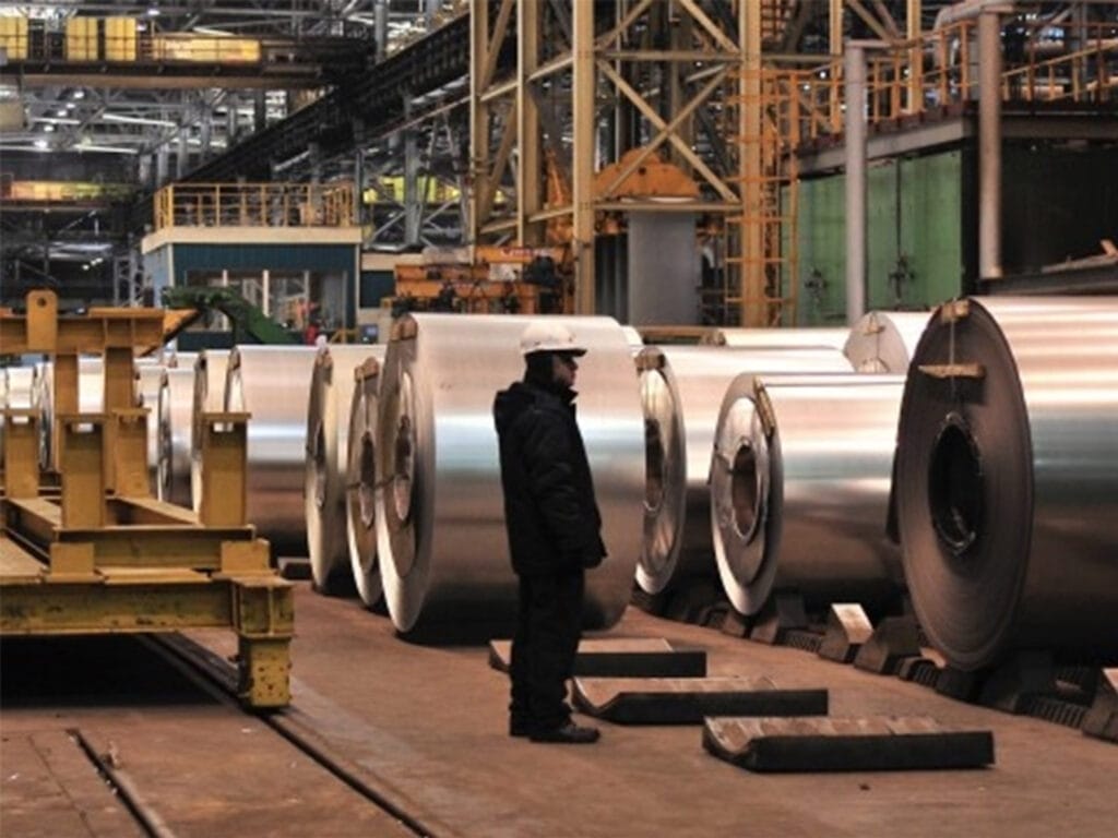 Worker inspecting stacked grain-oriented silicon steel coils in NLMK's finished goods warehouse