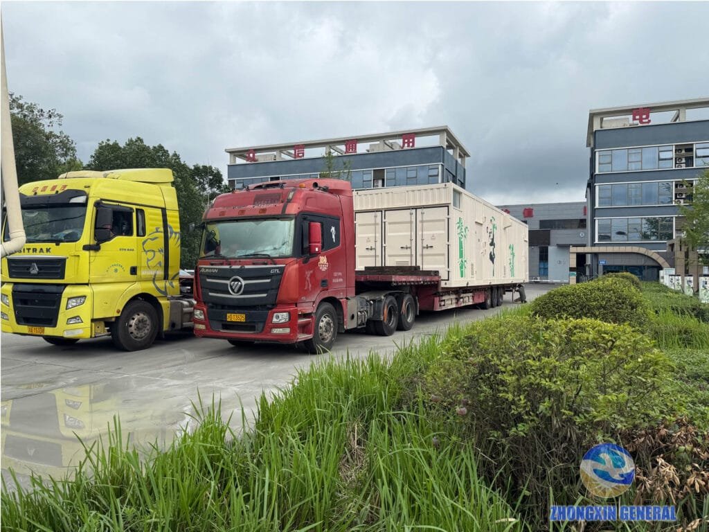 Two flatbed trucks positioned in the yard ahead of cargo securing for prefabricated switchgear cabin delivery
