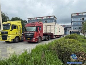 Two flatbed trucks positioned in the yard ahead of cargo securing for prefabricated switchgear cabin delivery