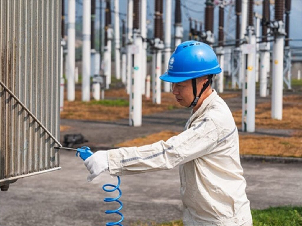 Worker uses dry compressed air to blow dust on outdoor oil immersed transformer radiator