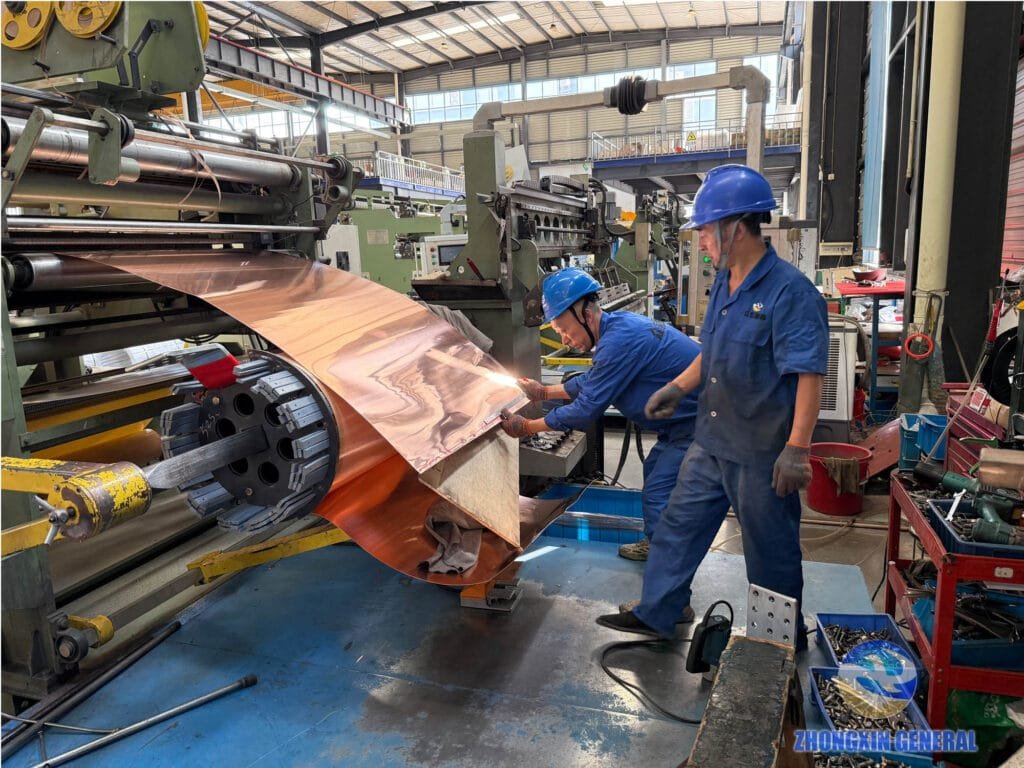 two technicians winding copper foil low voltage winding on foil winding machine during transformer production
